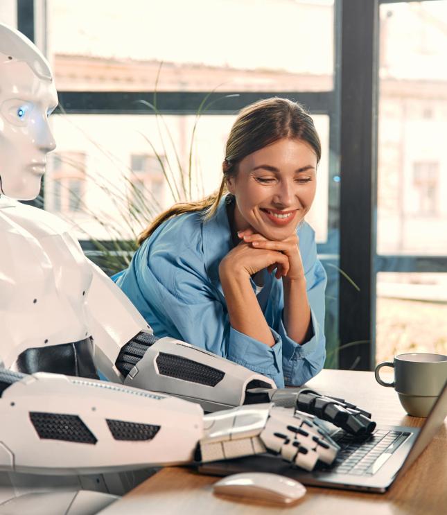 Young woman with a cup of coffee and a humanoid robot working while sitting at a laptop in a modern office. Collaboration between humans and artificial intelligence.