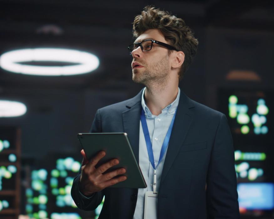 Serious IT specialist working tablet computer in data center closeup. Successful businessman overlooking server farm cloud computing facility typing digital device screen. Man looking asides at work